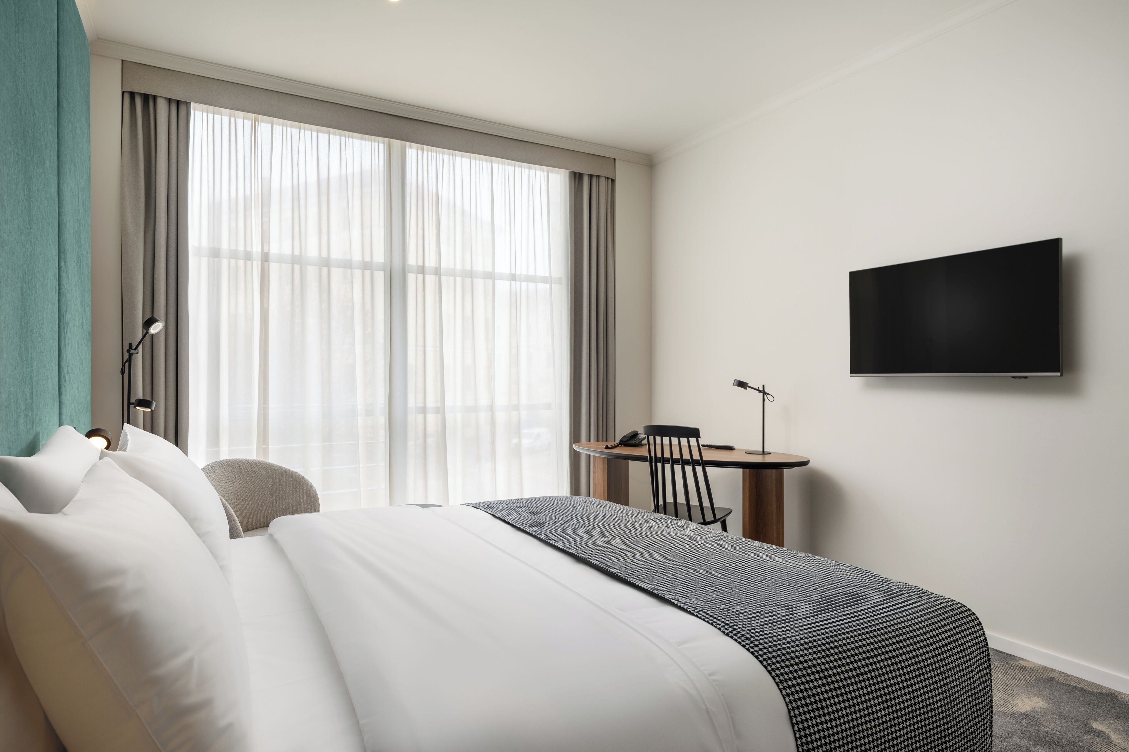 Una habitación de hotel moderna con una cama grande, un escritorio y un televisor montado en la pared.