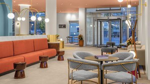 A modern lobby with a red sofa, grey chairs, a round table, and a glass elevator. - Hotel Lycium Debrecen - Handwritten Collection (Debrecen)