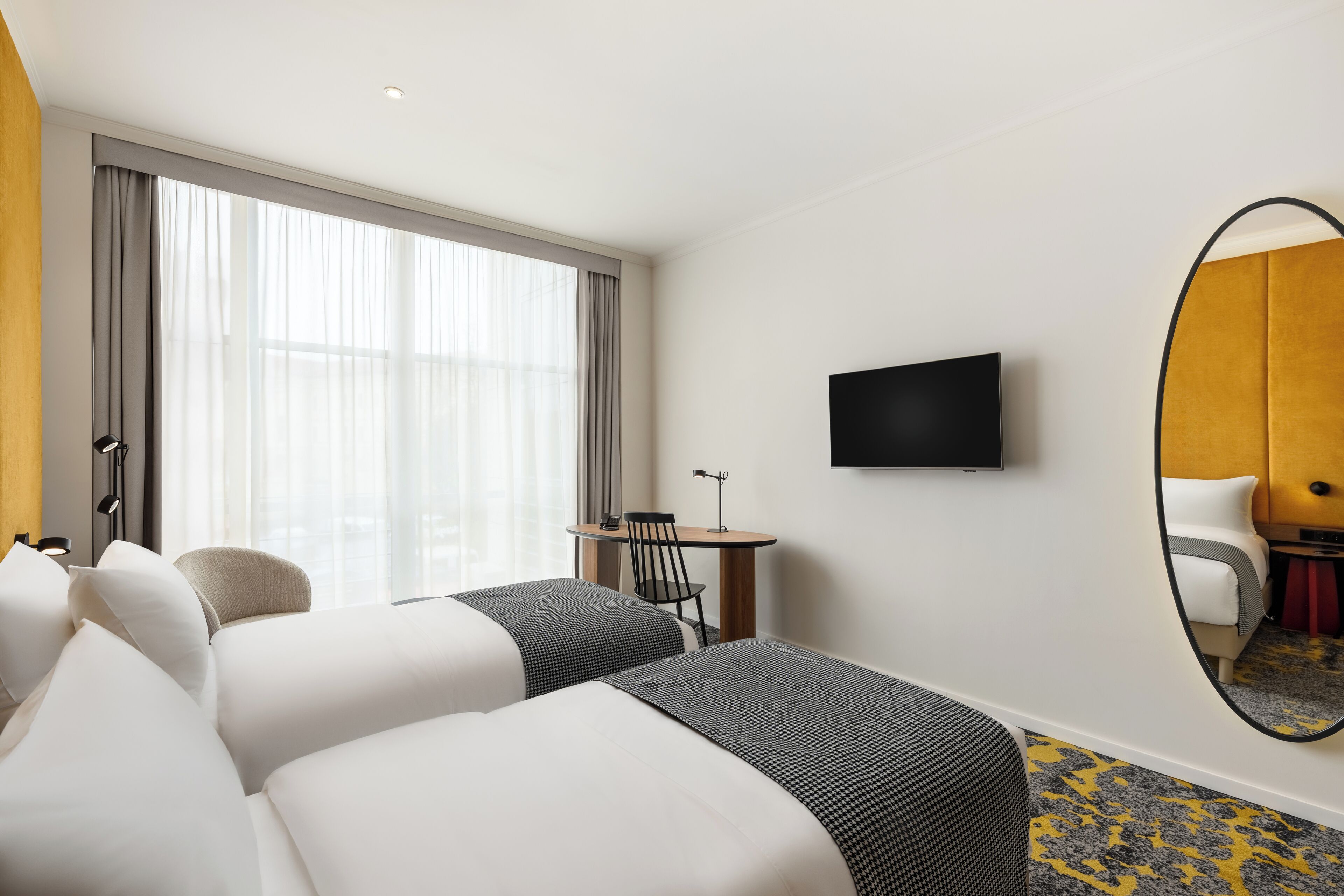 Ein Hotelzimmer mit zwei Betten, einem Schreibtisch, einem Stuhl, einem Fernseher und einem großen Spiegel.