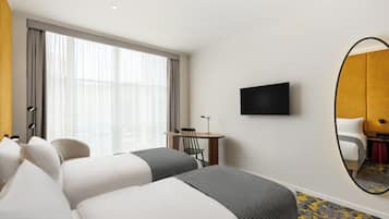 Ein Hotelzimmer mit zwei Betten, einem Schreibtisch, einem Stuhl, einem Fernseher und einem großen Spiegel.