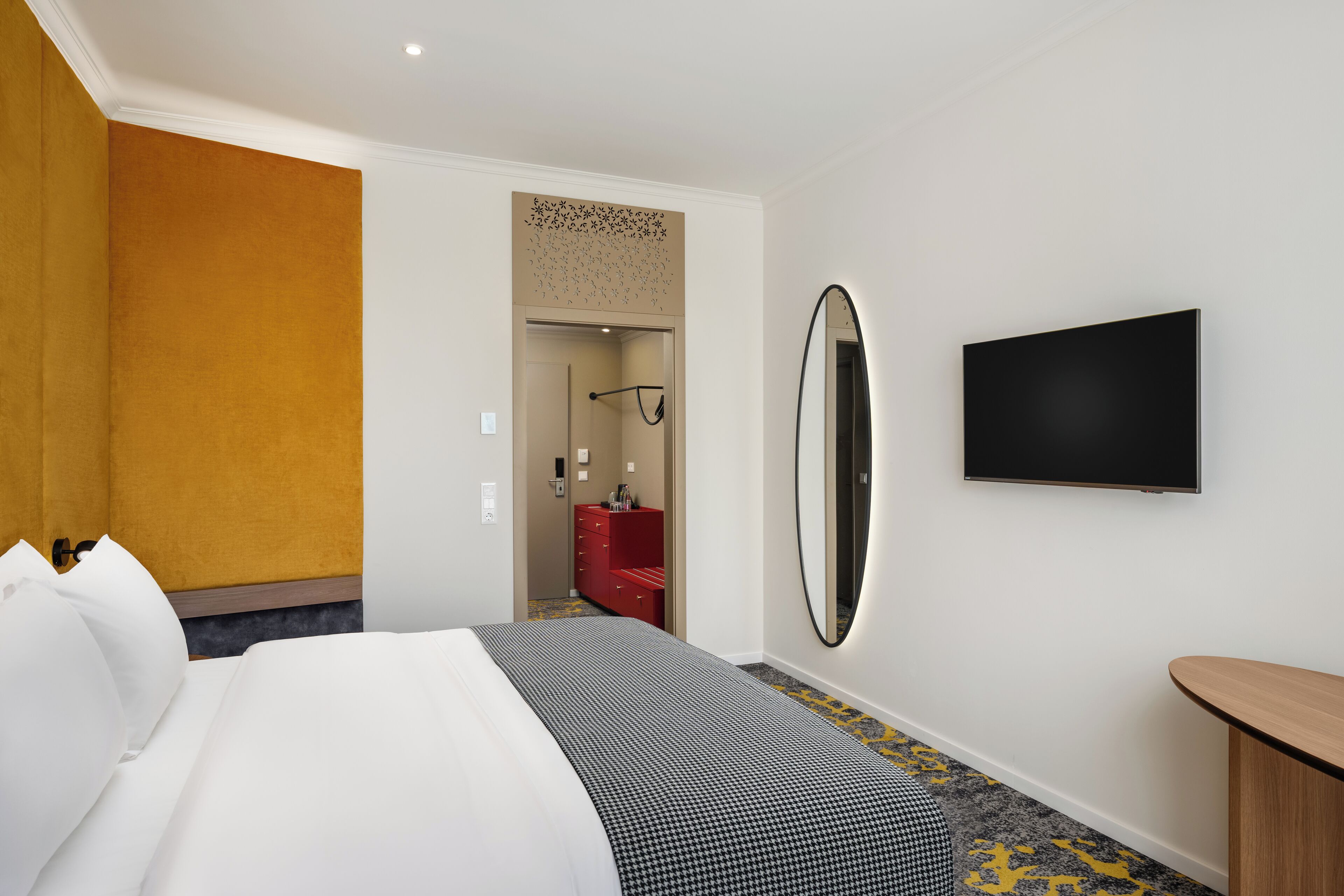 Een hotelkamer met een bed, een televisie, een spiegel en een rode ladekast.