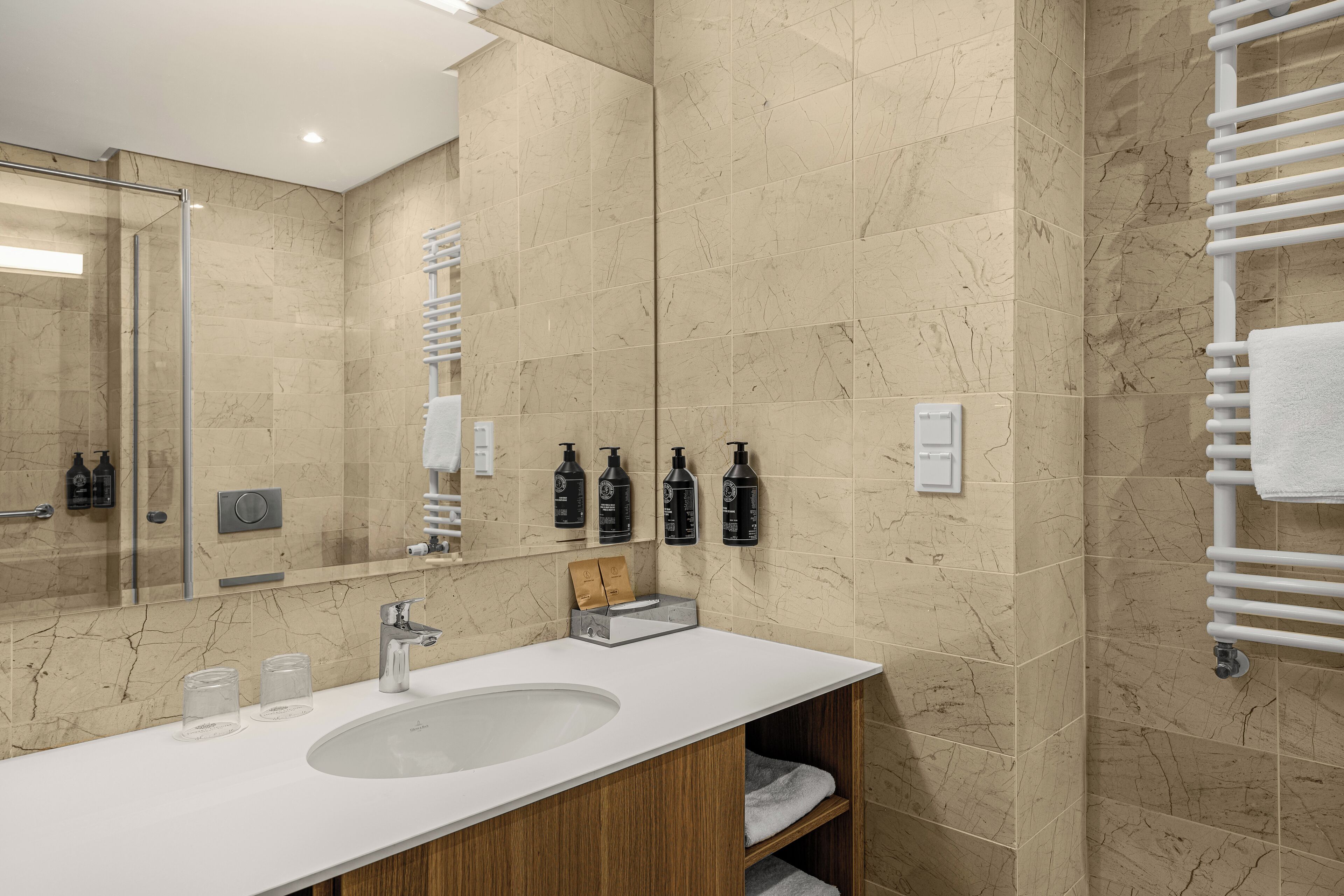 Een moderne badkamer met een betegelde wand van marmer, een witte wastafel en een grote spiegel.