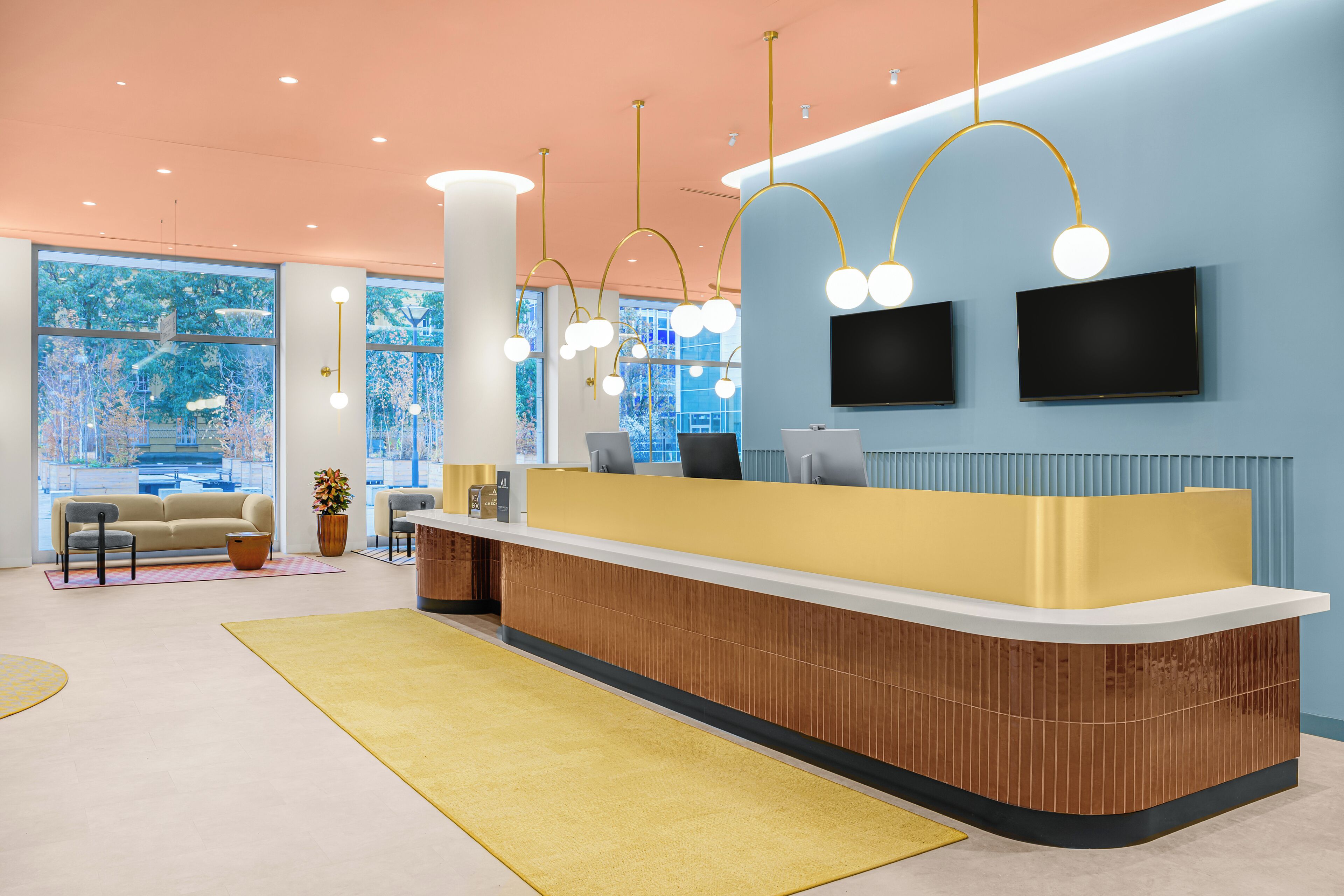 A modern reception area with a curved reception desk, two flat-screen TVs, and a large window with a view of trees.