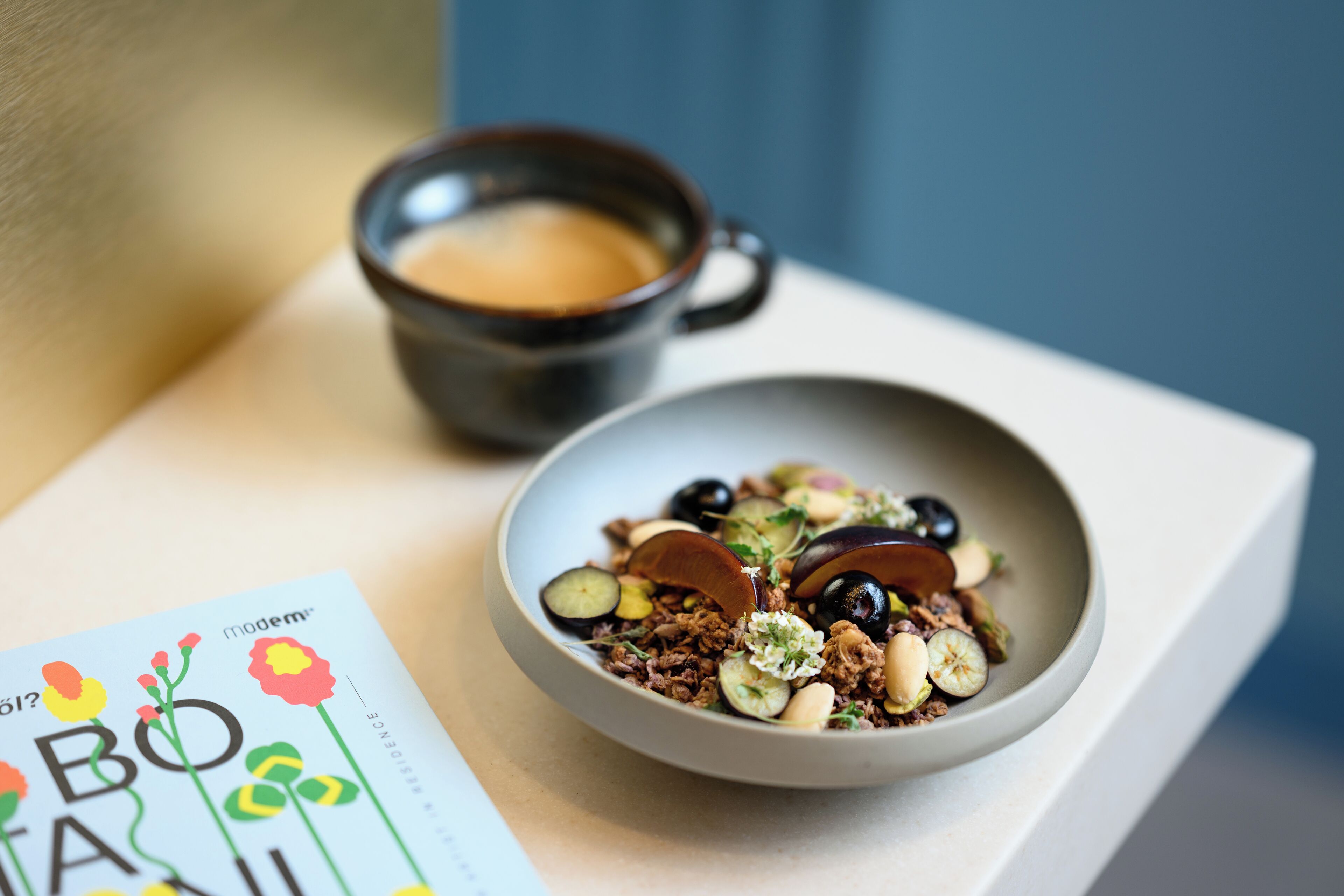A bowl of salad with various ingredients, a cup of coffee, and a book on a table.