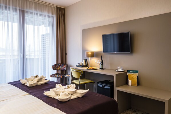 A hotel room with a bed, a desk, a chair, a TV, and a window with curtains. - Hotel Golden Lake Resort (Balatonfured)