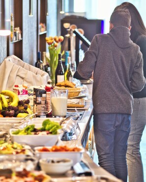 Ein reichhaltiges Buffet mit verschiedenen Speisen und Getränken, ein Sofa und im Hintergrund ein Fernseher.