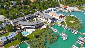 Vue aérienne d’une marina avec des bateaux amarrés, une piscine et un bâtiment doté d’un toit incurvé.