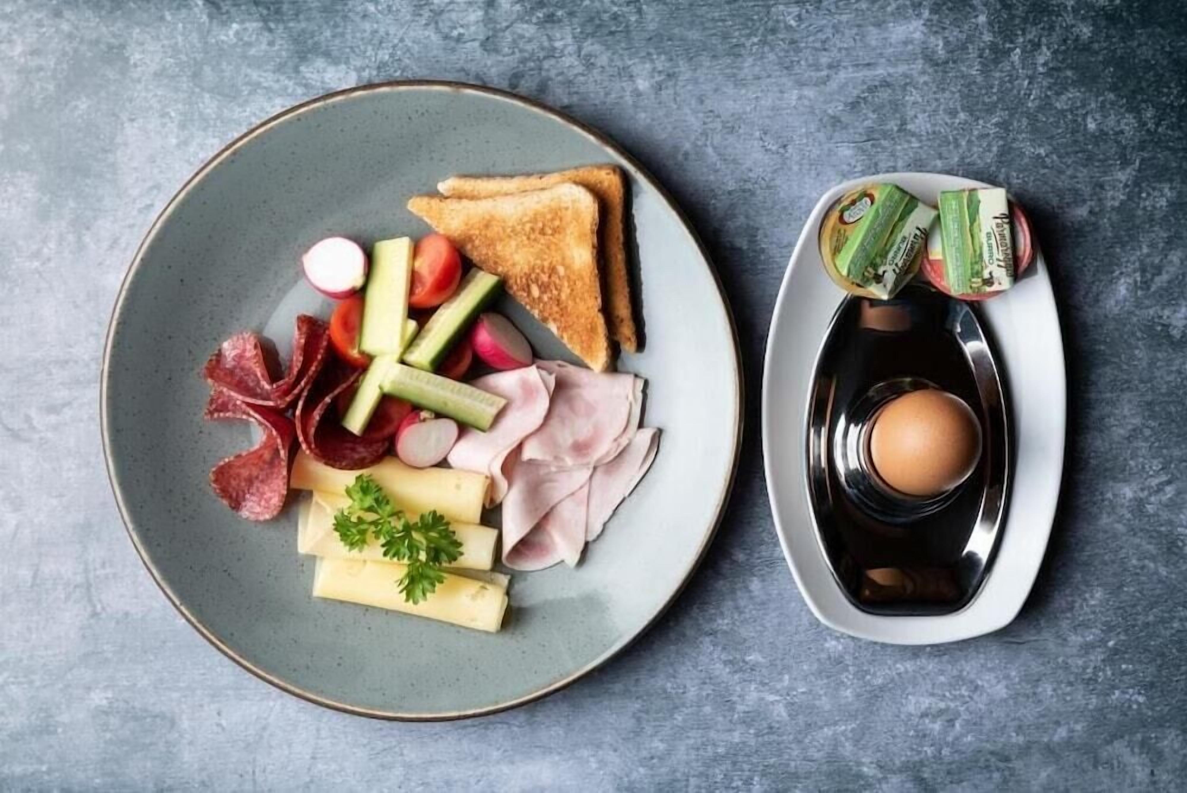Ein Teller mit Toast, verschiedenen Fleischsorten, Käse und Gemüse, sowie ein weiterer Teller mit einem gekochten Ei und Beilagen.