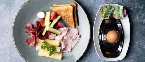 Ein Teller mit Toast, verschiedenen Fleischsorten, Käse und Gemüse, sowie ein weiterer Teller mit einem gekochten Ei und Beilagen.
