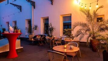 Un patio al aire libre con mesas y sillas redondas, luces colgantes y plantas en macetas.
