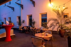 An outdoor patio area with round tables and chairs, string lights, and potted plants. - Concordia Hotel Targu Mures (Tirgu Mures)