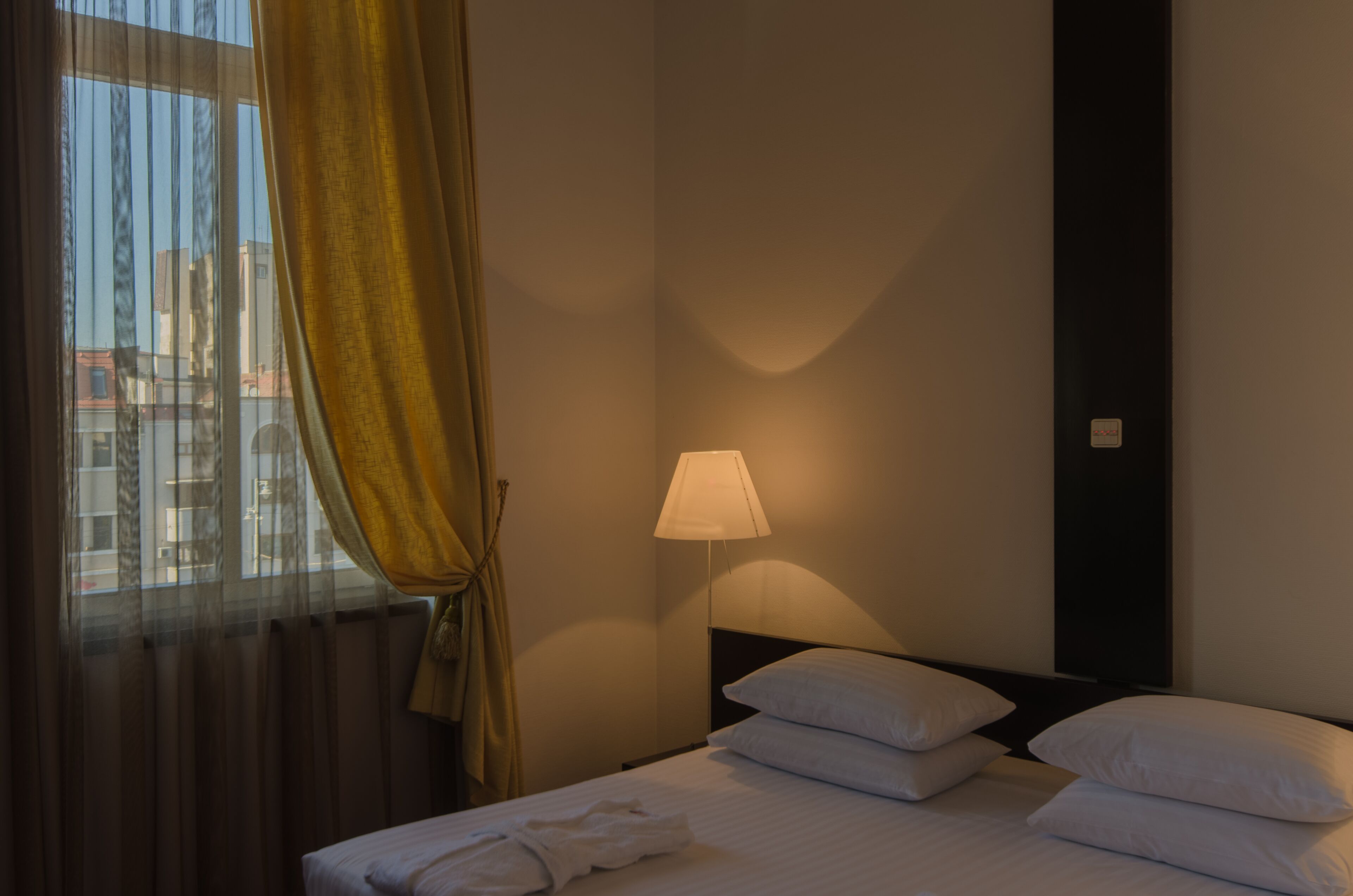 A hotel room with a bed, a nightstand, a lamp, and a window with curtains.
