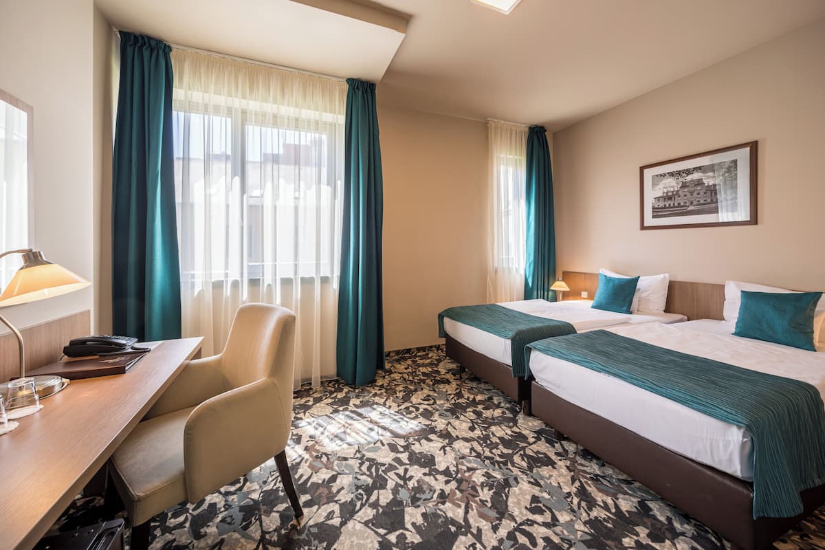 Una habitación de hotel con dos camas, un escritorio, una silla y un ventanal con cortinas.