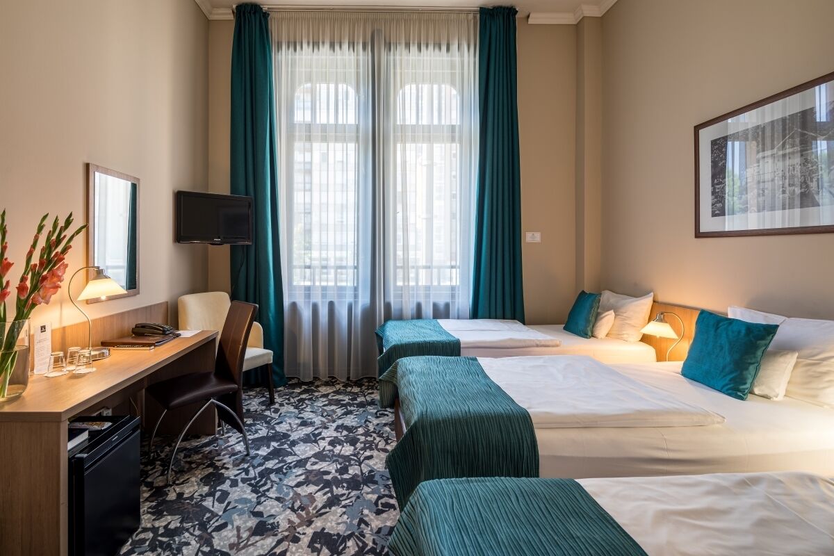 Una habitación de hotel con dos camas, un escritorio, una silla, un televisor y una ventana con cortinas.