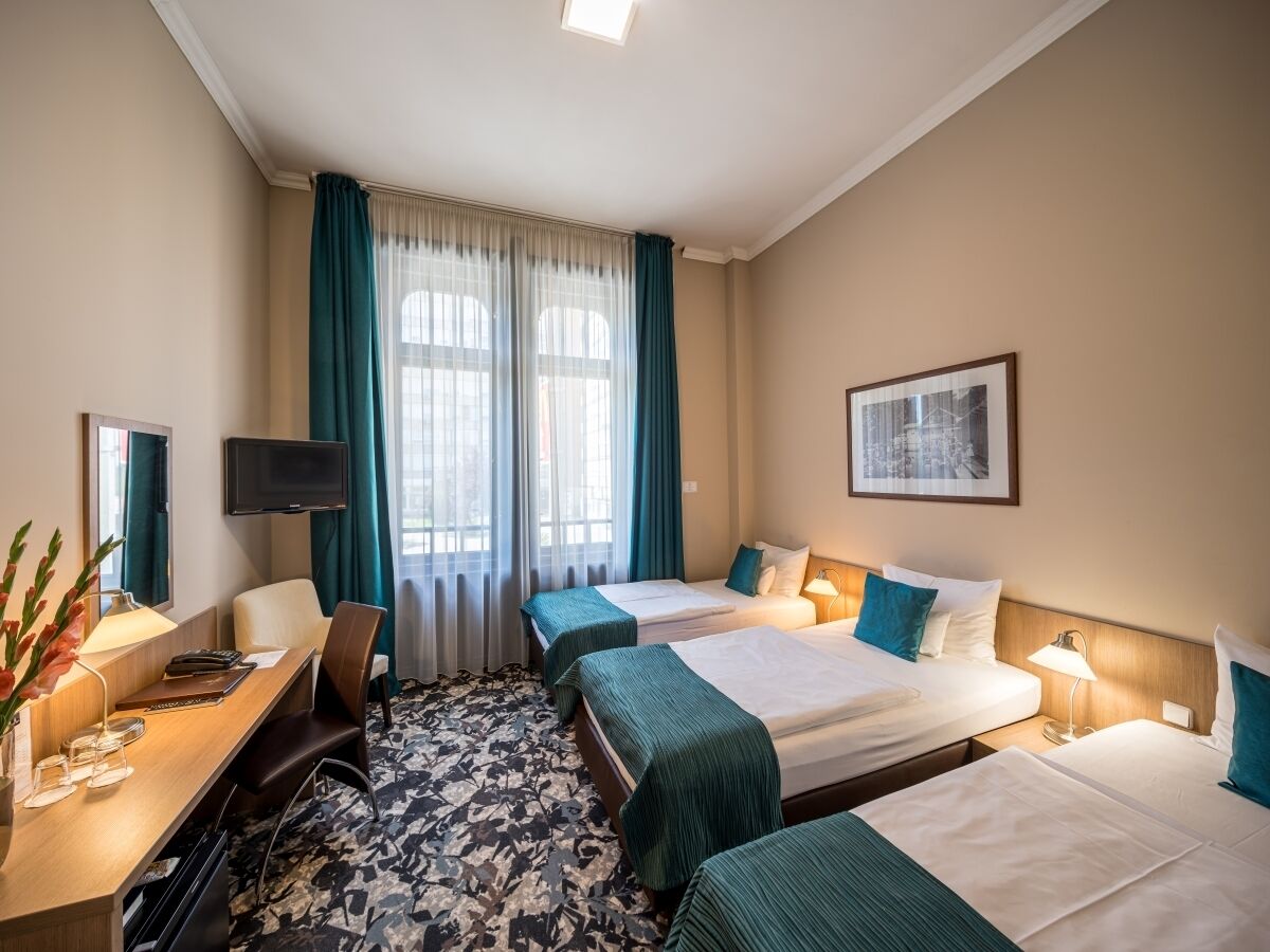 A hotel room with two beds, a desk with a chair, a TV, and a large window with curtains.