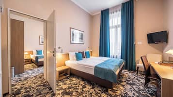 Habitación de hotel con una cama grande, un escritorio con silla, televisor montado en la pared y una ventana con cortinas.
