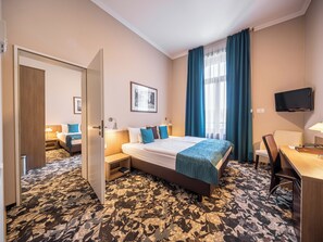 Une chambre d’hôtel avec un grand lit, un bureau avec une chaise, un téléviseur fixé au mur et une fenêtre avec des rideaux.