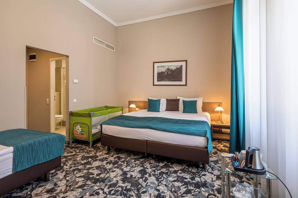 Una habitación de hotel con cama, sofá verde, escritorio con lámpara y un cuadro enmarcado en la pared.