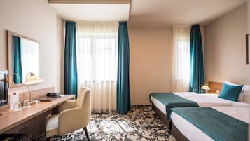 A hotel room with a desk, chair, two beds, and a large window with curtains.