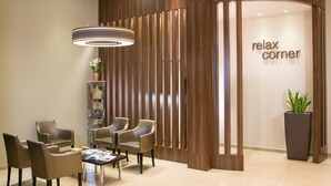 Un espace d’accueil avec un panneau indiquant un « coin détente », un luminaire moderne et un aménagement avec des chaises et une table.