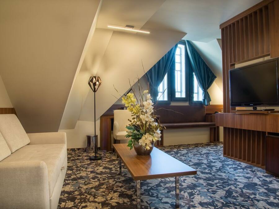 Una sala moderna con un sofá, una mesa de centro con flores, un televisor y un amplio ventanal con cortinas.