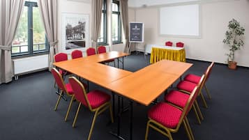 Una sala de conferencias con una gran mesa de madera, sillas rojas, una pantalla de proyector y un mantel amarillo.