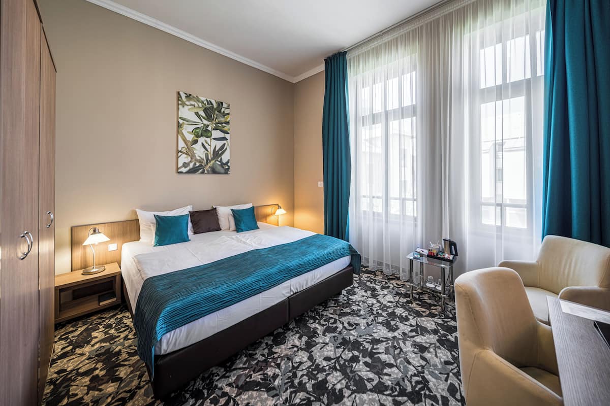 Una habitación de hotel con una cama grande, un escritorio, una silla, una mesita de noche y una lámpara de pared.