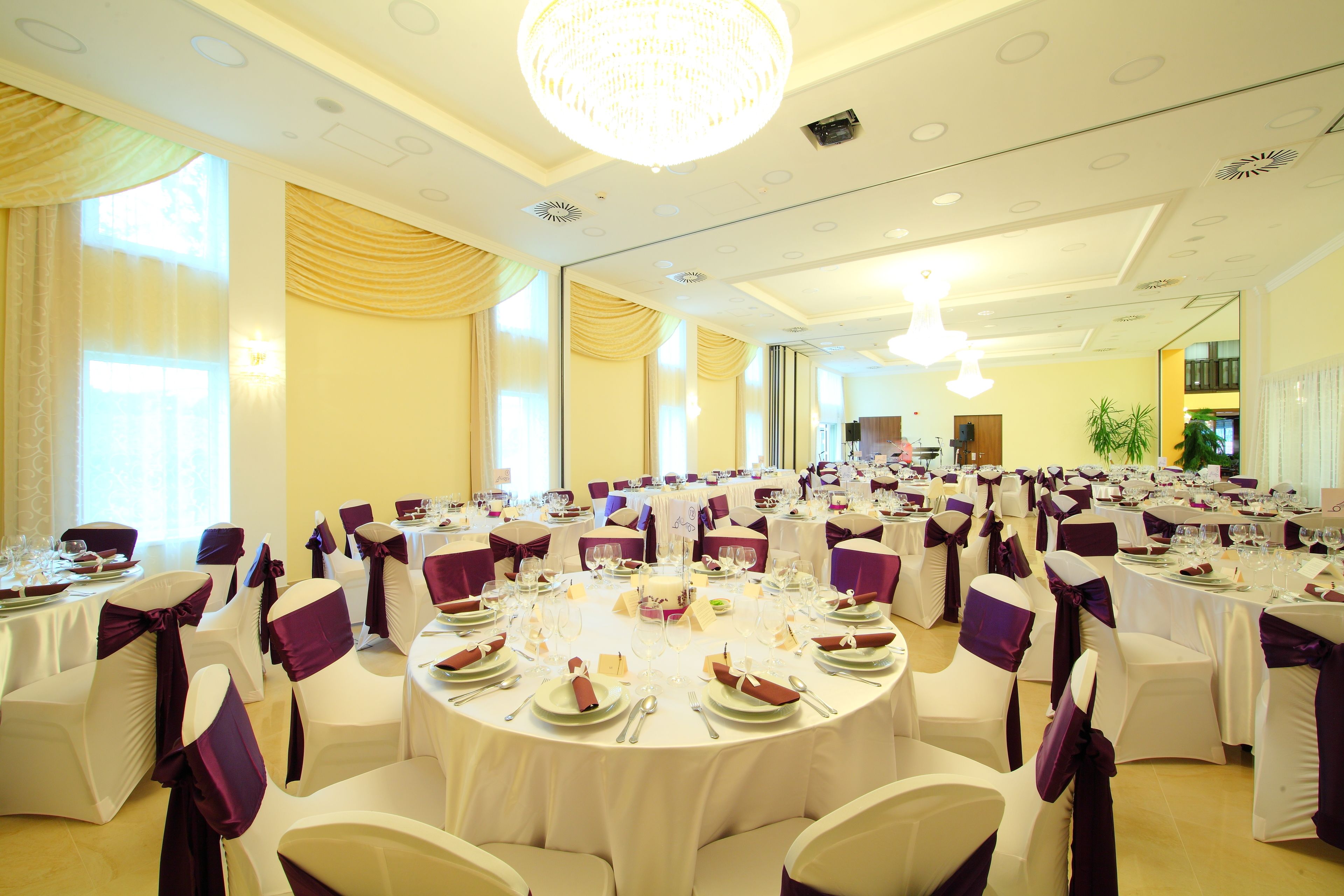 A banquet hall with round tables, white chairs, and purple sashes.