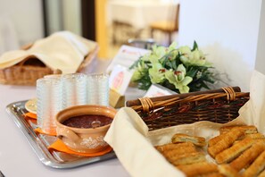 Una mesa de buffet con diversos alimentos, incluyendo un bol de salsa, una cesta de pan y una bandeja de bebidas.