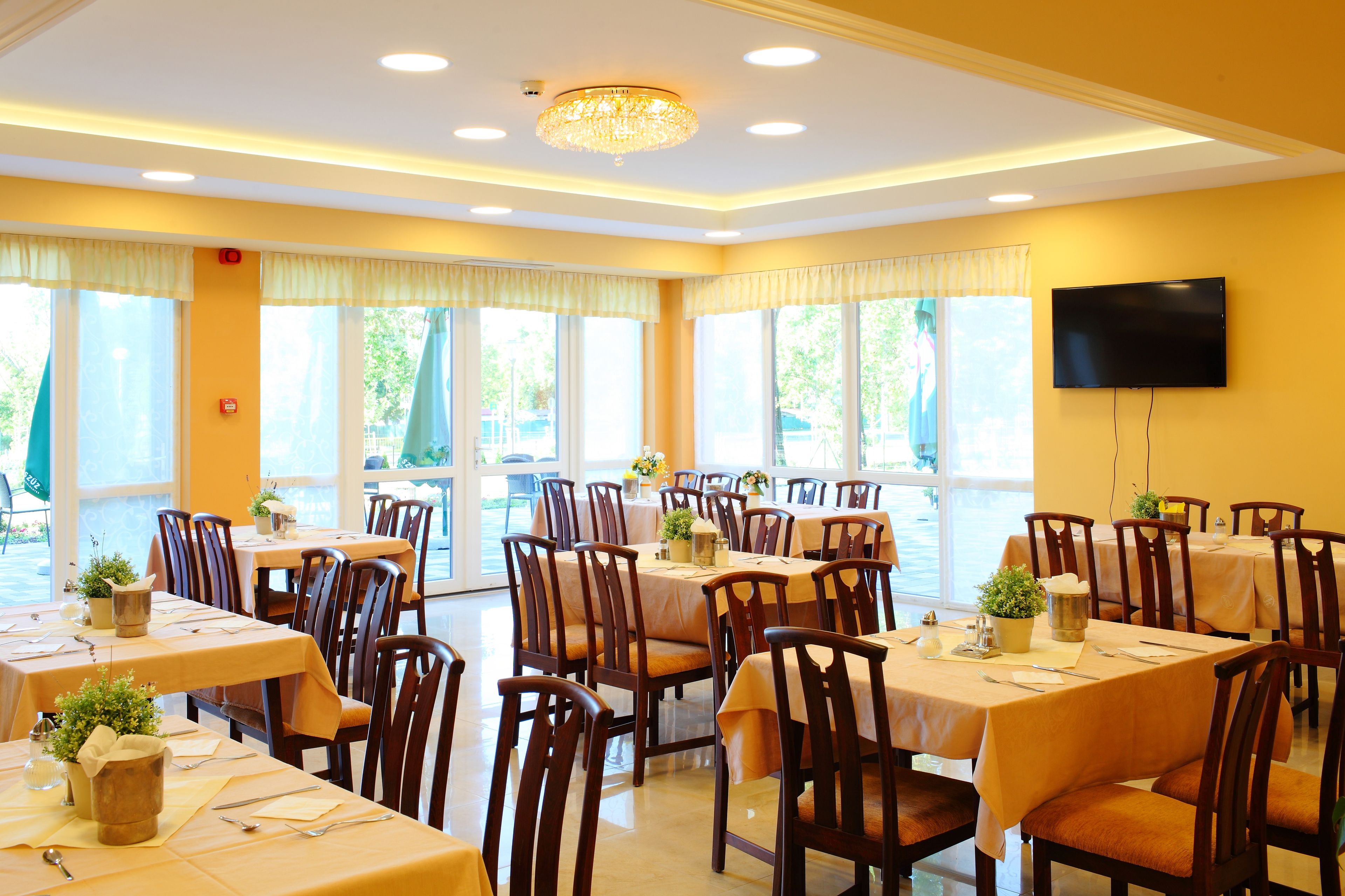 A dining area with multiple tables and chairs, large windows, and a chandelier.