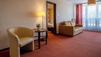 A hotel room with a beige armchair, a sofa, a small table with a plant, and a lamp.