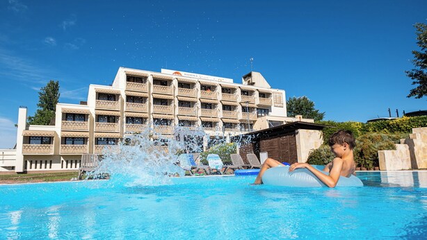 Et hotel med swimmingpool, et barn i poolen, og en bygning med skilt der siger "Business".