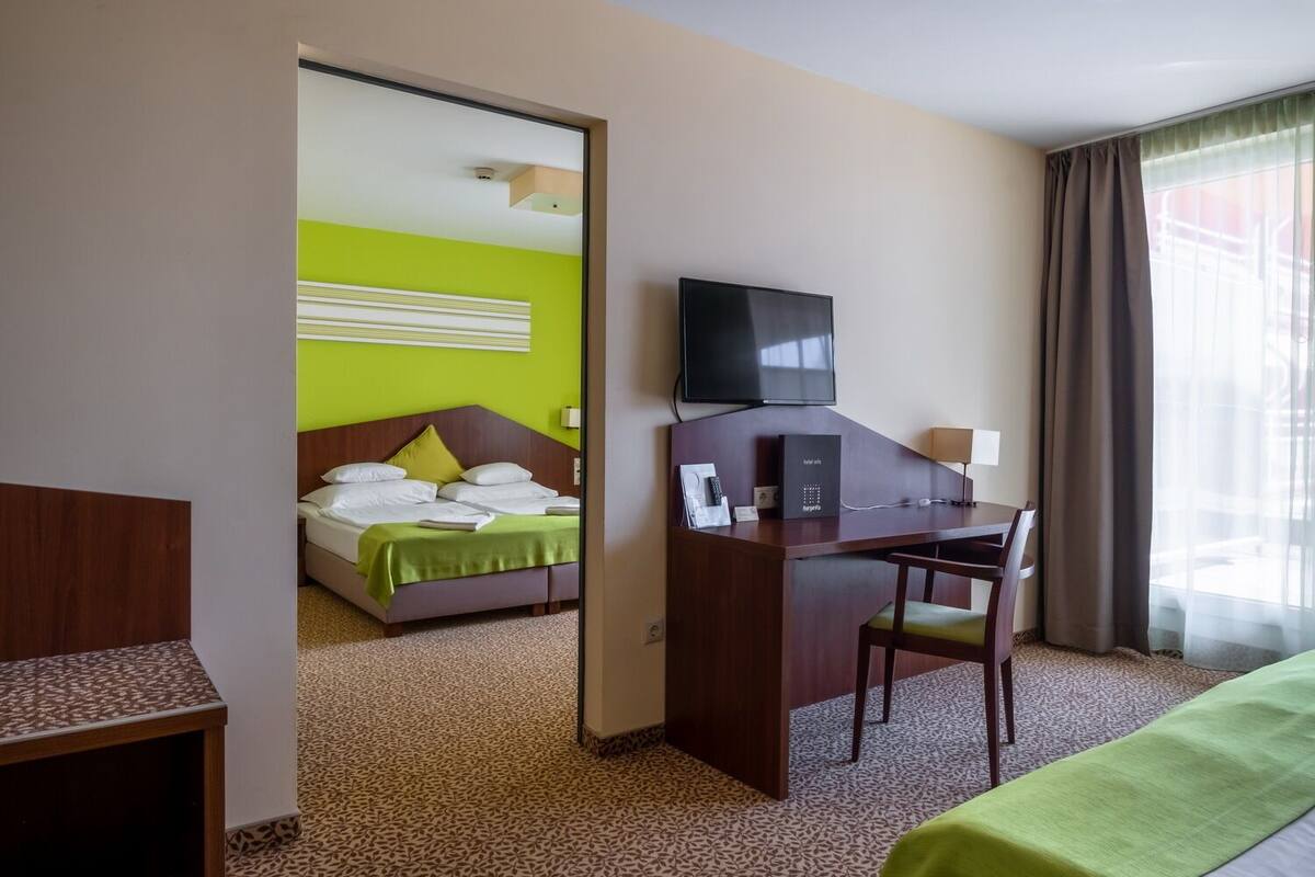 Une chambre d’hôtel avec un lit, un bureau, une télévision et une fenêtre avec des rideaux.