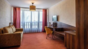A hotel room with a sofa, a desk, a chair, a television, and a large window with curtains.