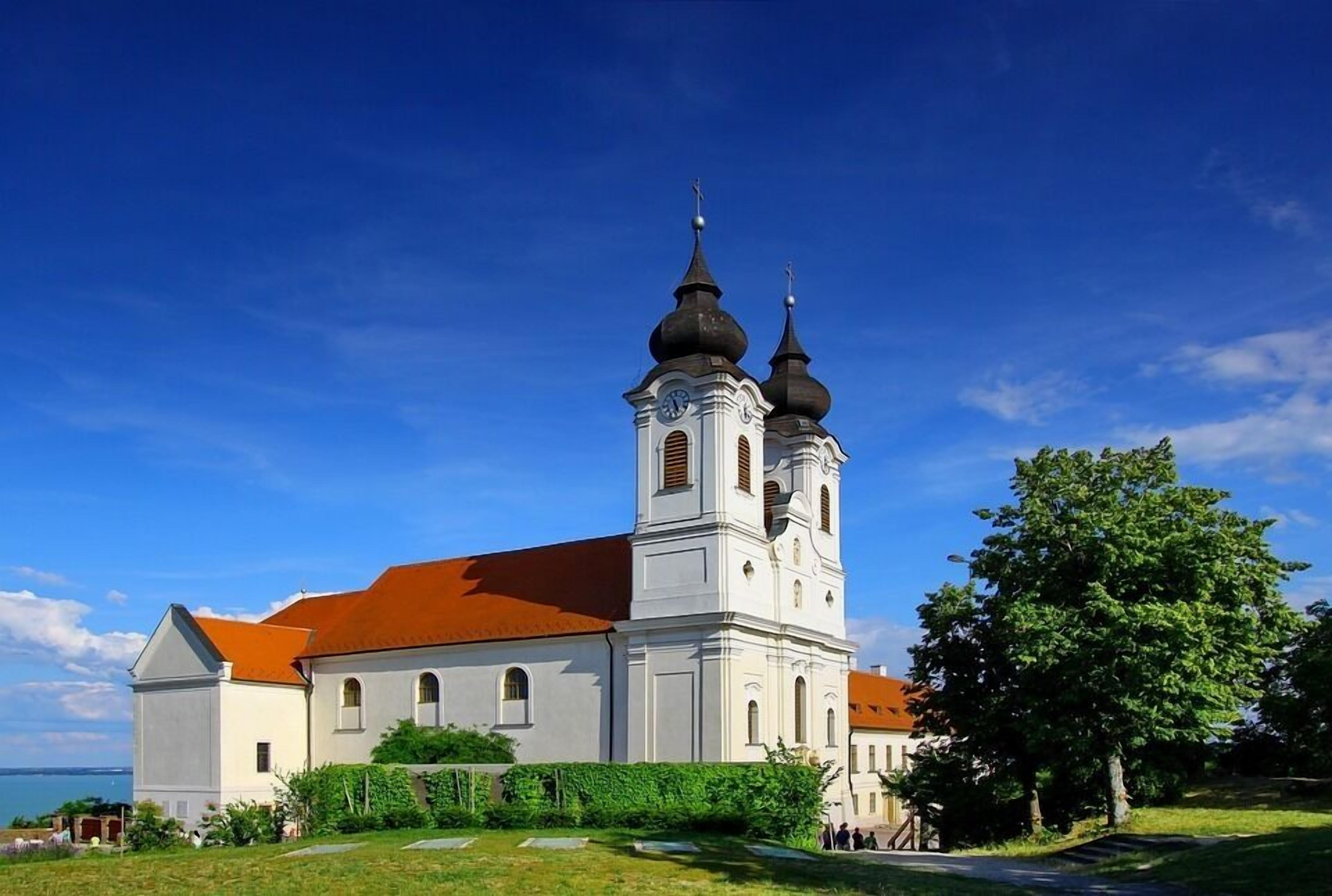 A white church with a red roof and two domes, surrounded by greenery.