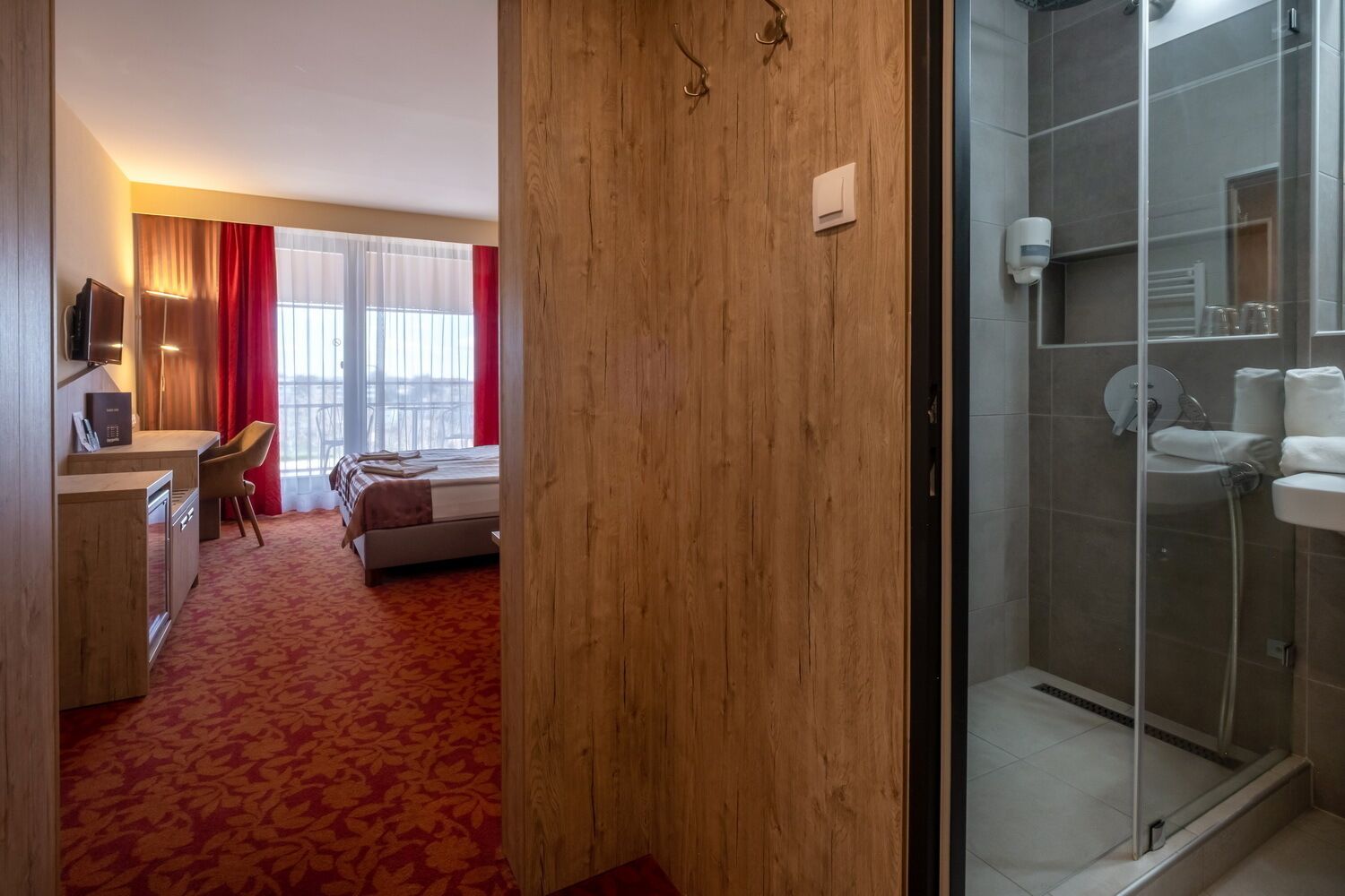 Quarto de hotel com cama, escrivaninha, cadeira, chuveiro e vista para o exterior.
