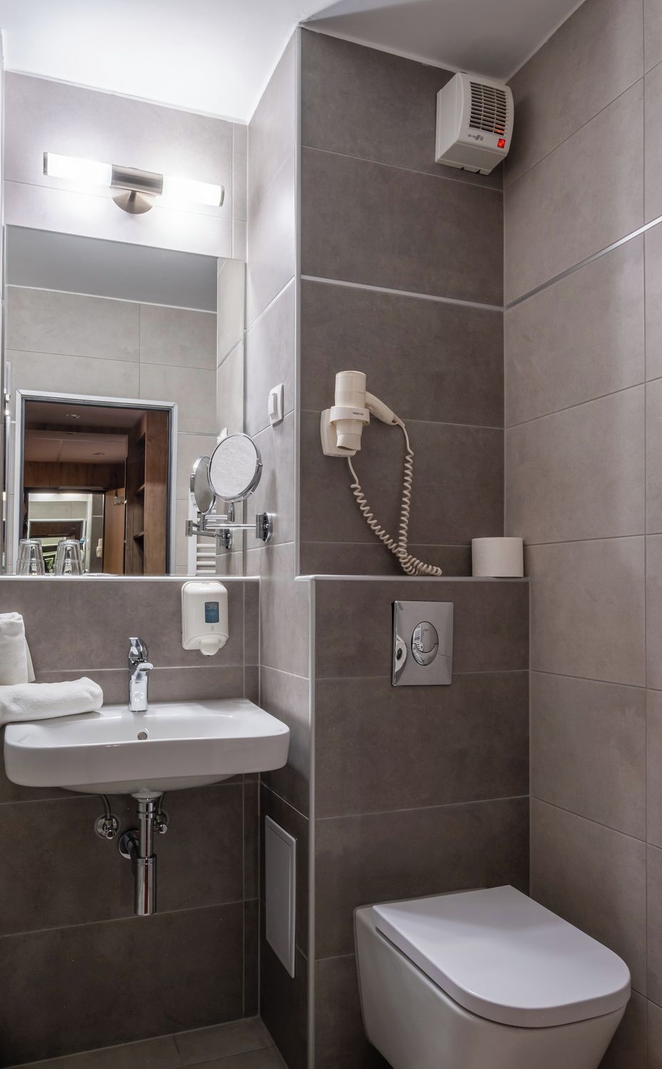 A modern bathroom with a sink, mirror, hairdryer, and toilet.