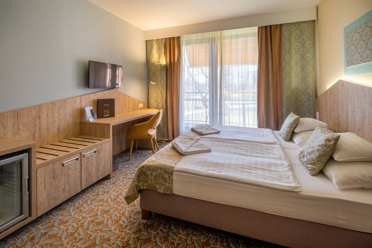 Une chambre d’hôtel équipée d’un lit, d’un bureau, d’une chaise, d’une télévision et d’une fenêtre avec des rideaux.