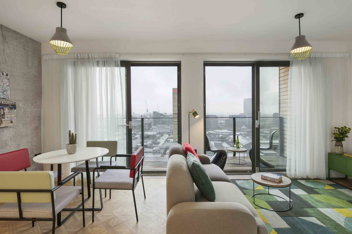 Una sala de estar moderna con un sofá, sillas, una mesita y un balcón con vistas a la ciudad.