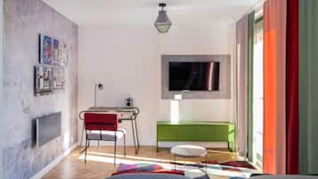 A modern living room with a flat-screen TV, a desk with a chair, a green cabinet, and a colorful rug.