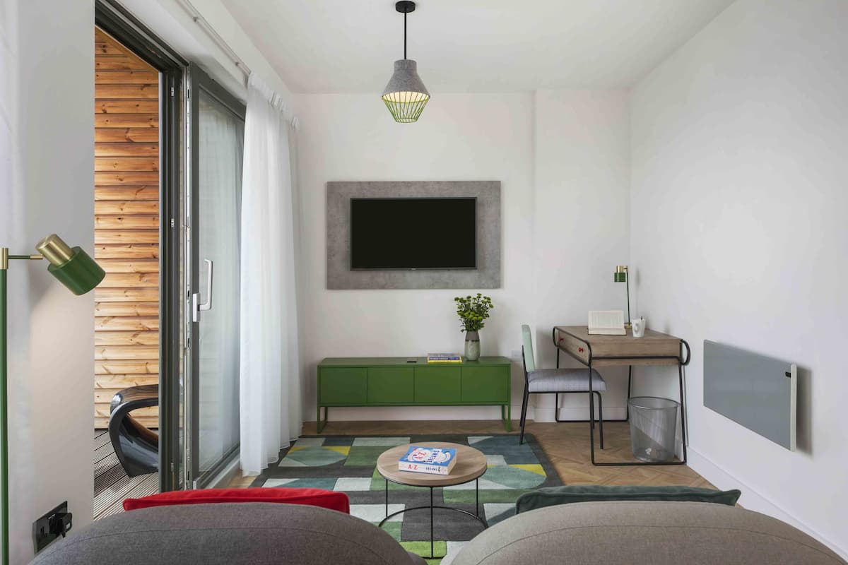 Una sala de estar moderna con un aparador verde, una mesa redonda de centro, un sofá, un televisor montado en la pared y una lámpara colgante.