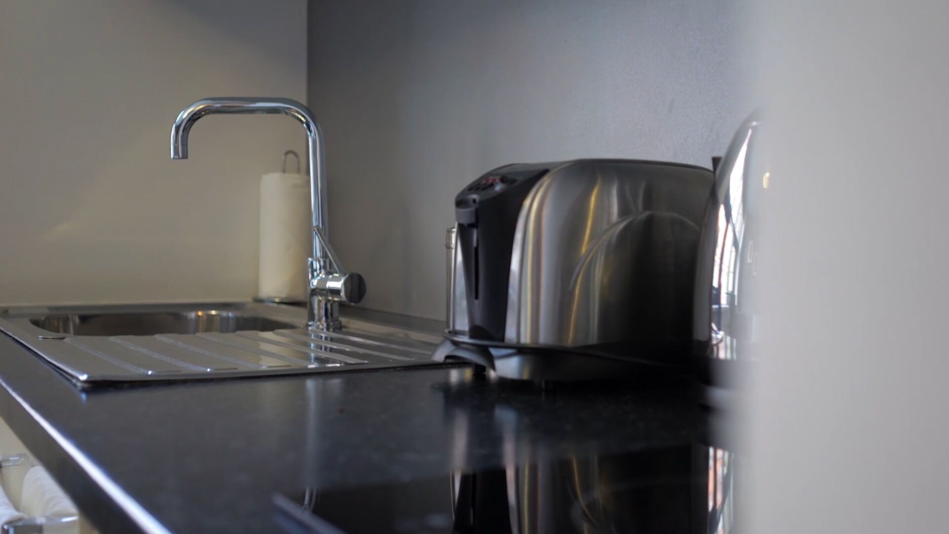 A kitchen with a stainless steel sink, a faucet, and a toaster on a black countertop.