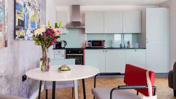 A modern kitchen with light green cabinets, a microwave, and a stove. There is a dining area with a round table and chairs, and a vase with flowers on the table.