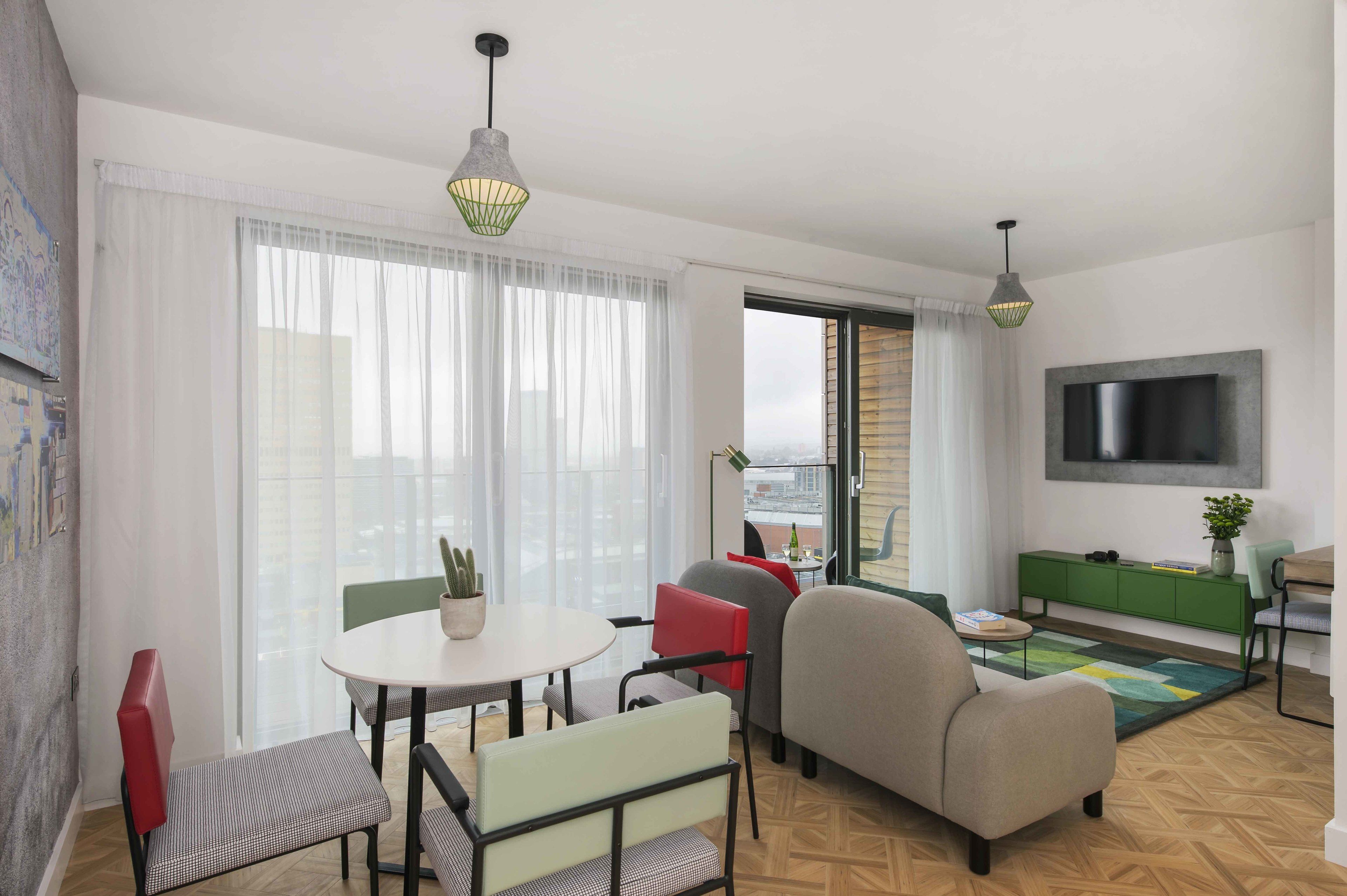 A modern living room with a round table, chairs, a sofa, a TV mounted on the wall, and a green cabinet.
