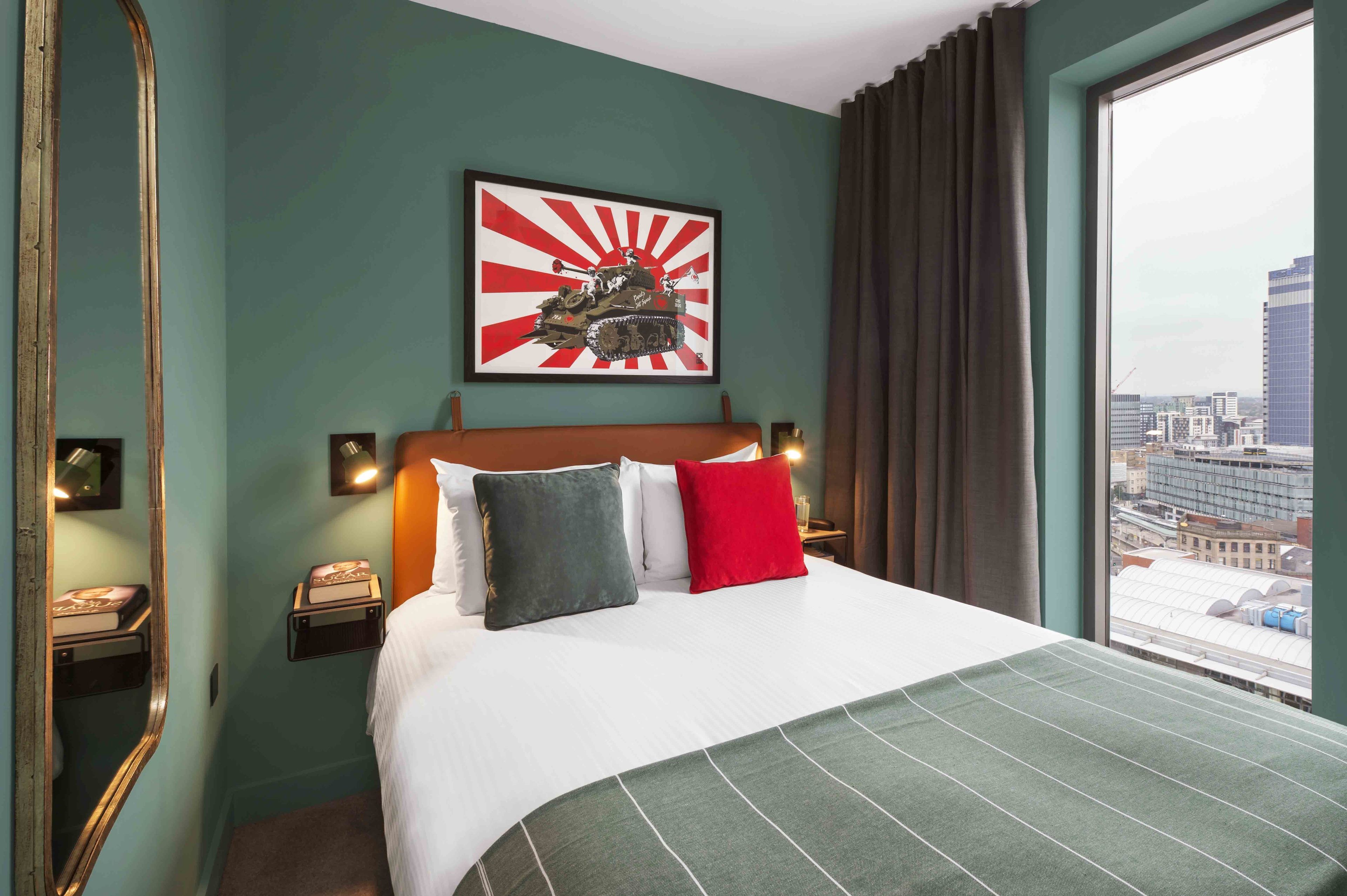 Une chambre d’hôtel avec un grand lit, une vue sur la ville, un tableau encadré au mur et un miroir.