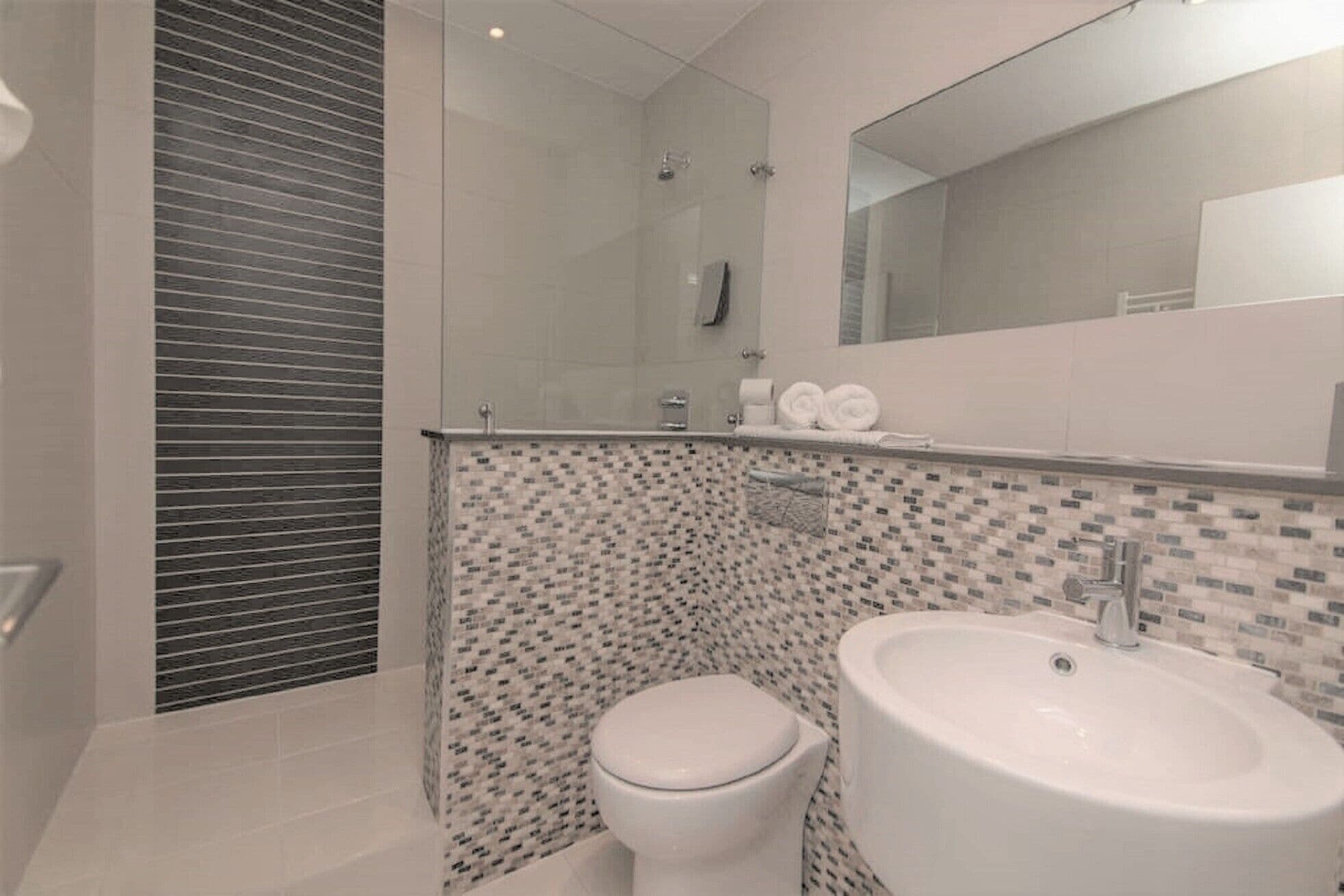 Een moderne badkamer met een glazen douchecabine, toilet en wastafel met spiegel erboven.