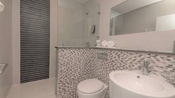 Een moderne badkamer met een glazen douchecabine, toilet en wastafel met spiegel erboven.