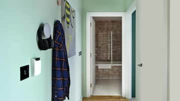 A hallway with a light green wall, a blue plaid jacket hanging on the wall, a white towel rack, and a bathroom visible through an open door.
