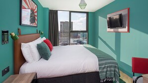 Habitación de hotel moderna con una cama grande, un televisor montado en la pared y vistas a la ciudad a través de la ventana.