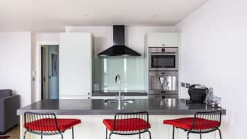 A modern kitchen with a central island, stainless steel appliances, and three bar stools with red cushions.